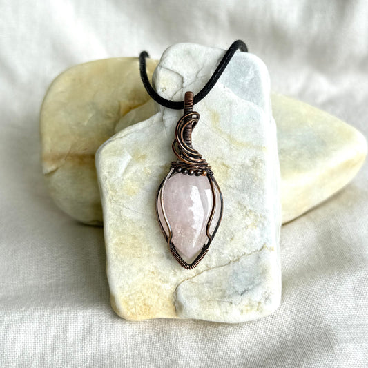 Copper pendant with a black cord on a piece of stone on linen background