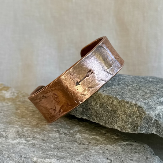 Copper bracelet with stamped arrow on it, leaning on a stone on linen background