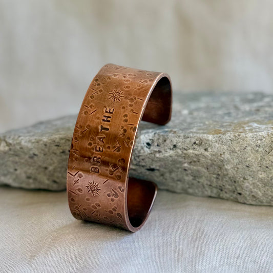 Copper cuff with 'BREATHE' engraving on a stone surface