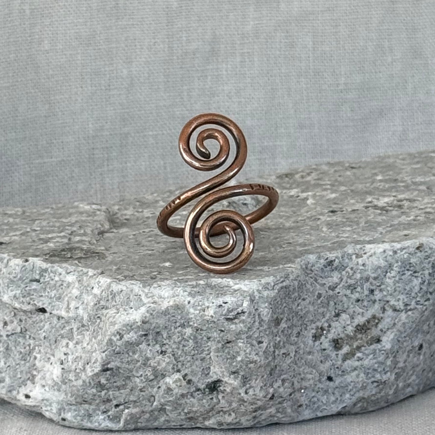 Copper spiral ring on a stone surface with a linen fabric background