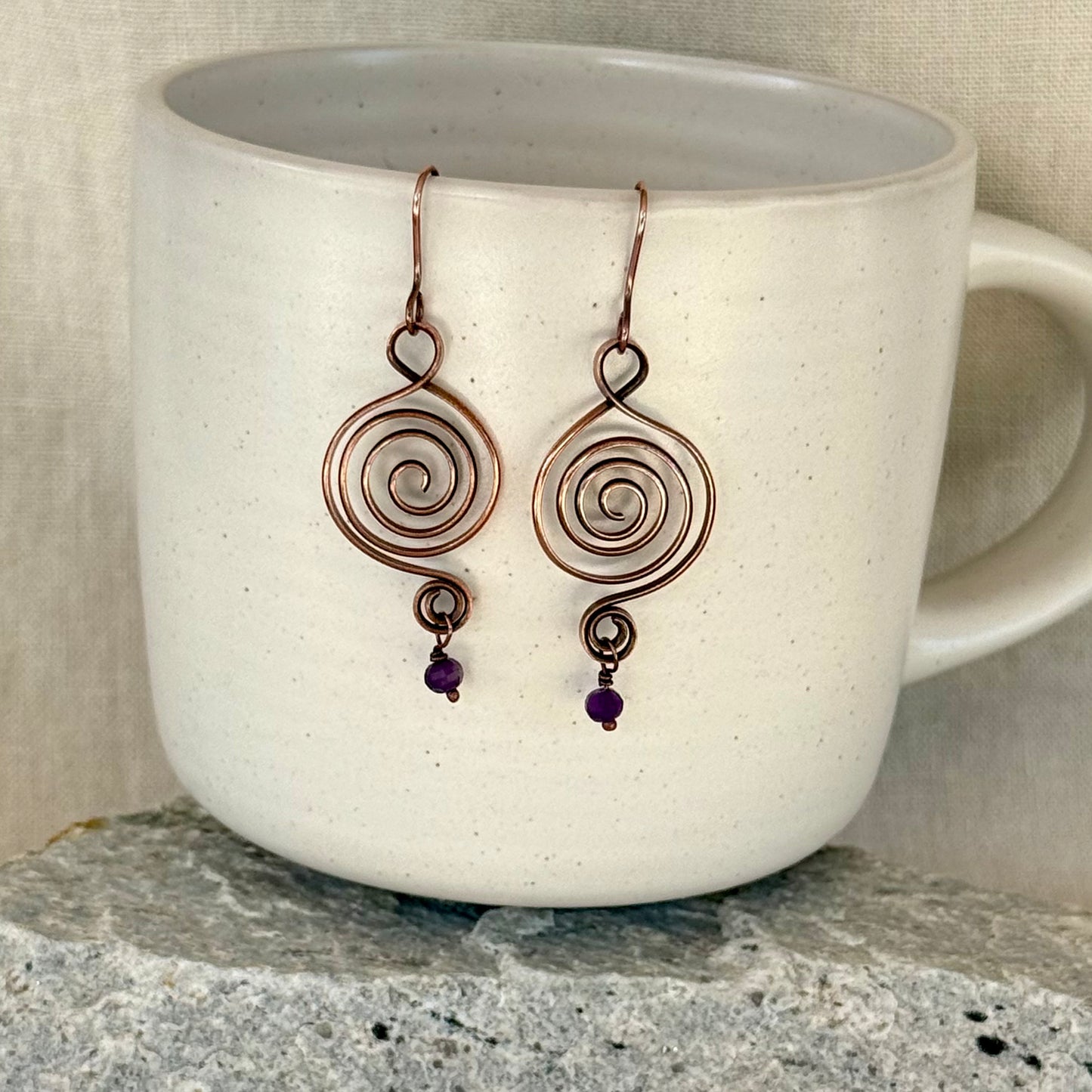 Pair of spiral earrings with purple beads on a white mug.