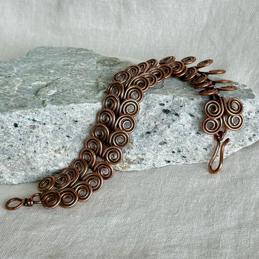 Copper bracelet with intricate spiral design on a stone and fabric background