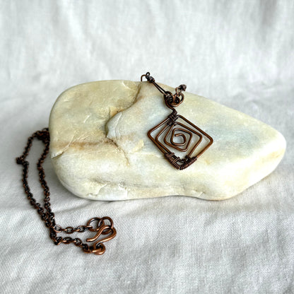 Copper necklace with a geometric pendant on a stone and white fabric background