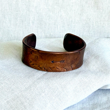 Copper bracelet with an arrow design on a white fabric background