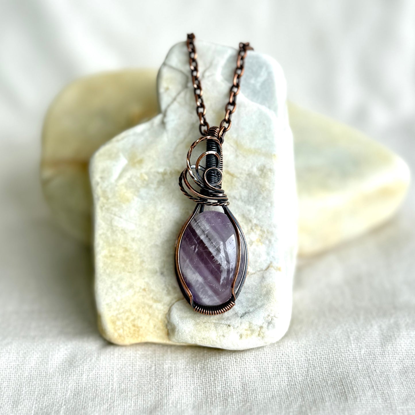 Copper pendant with a purple Amathyst stone on a piece of stone on linen background