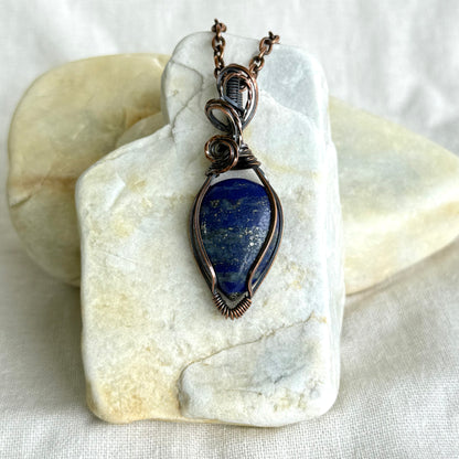 Copper pendant with blue stone and a black cord on a piece of stone on linen background