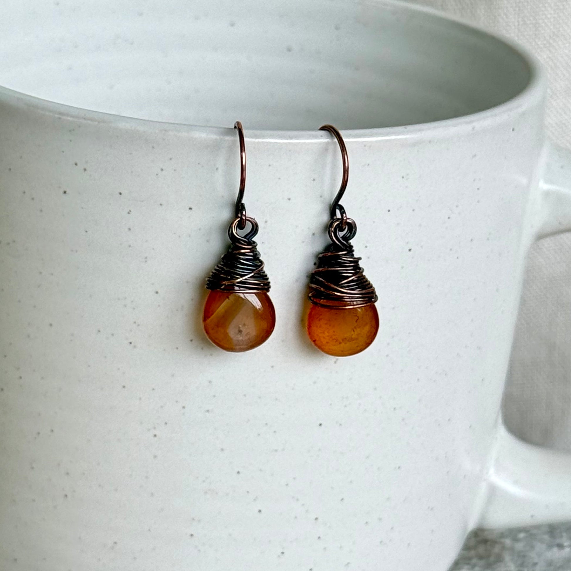 Pair of copper and carnelian teardrop earrings on a white ceramic cup
