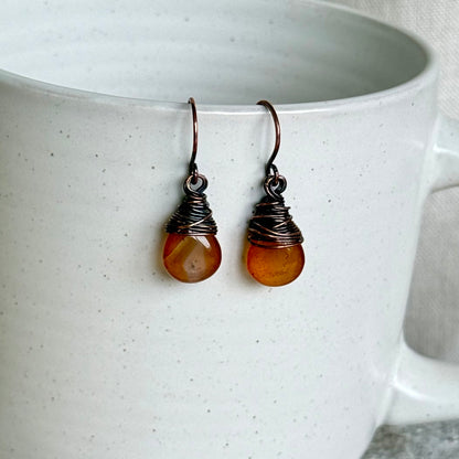 Pair of copper and carnelian teardrop earrings on a white ceramic cup