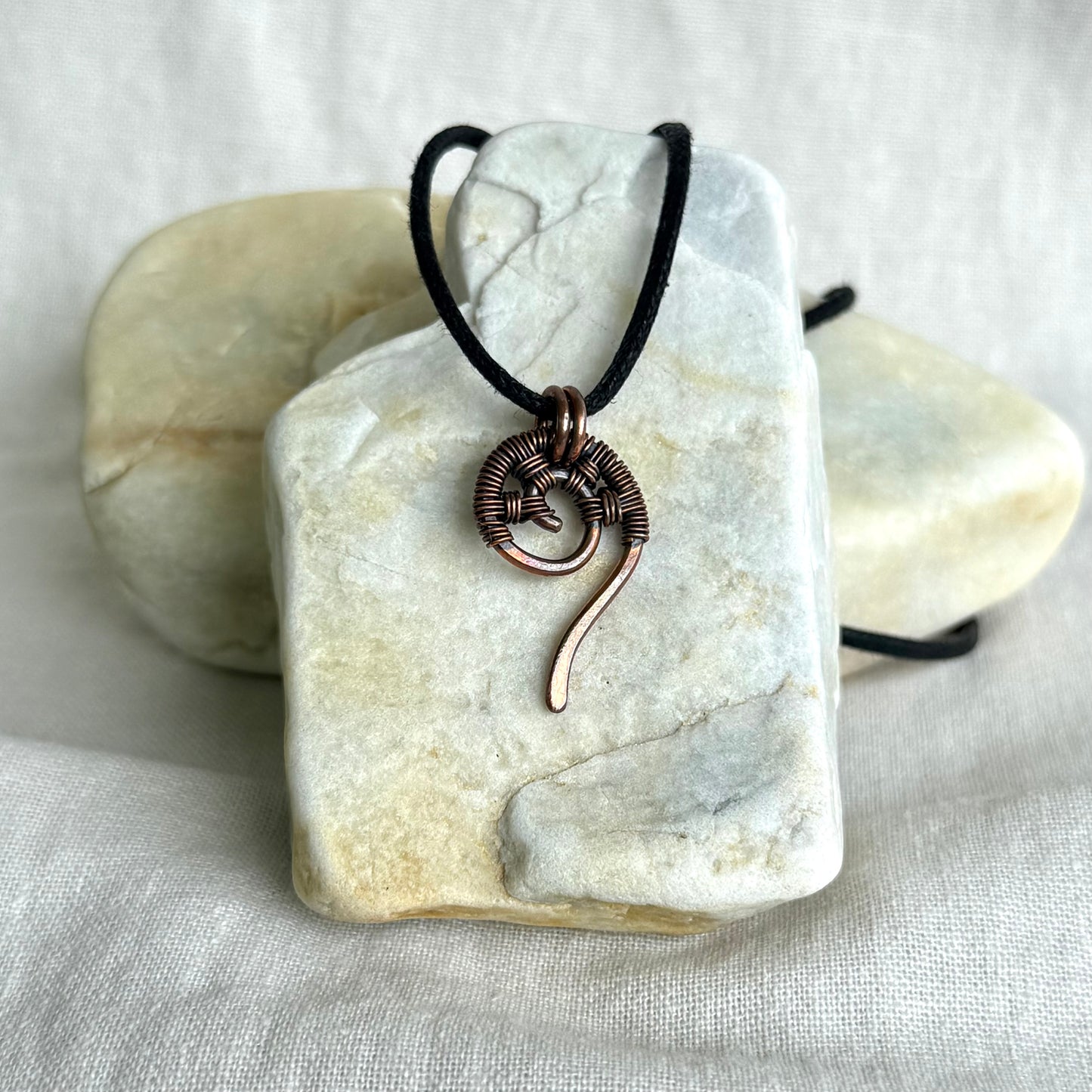 Copper wire-wrapped pendant on a black cord, displayed on a white stone surface.