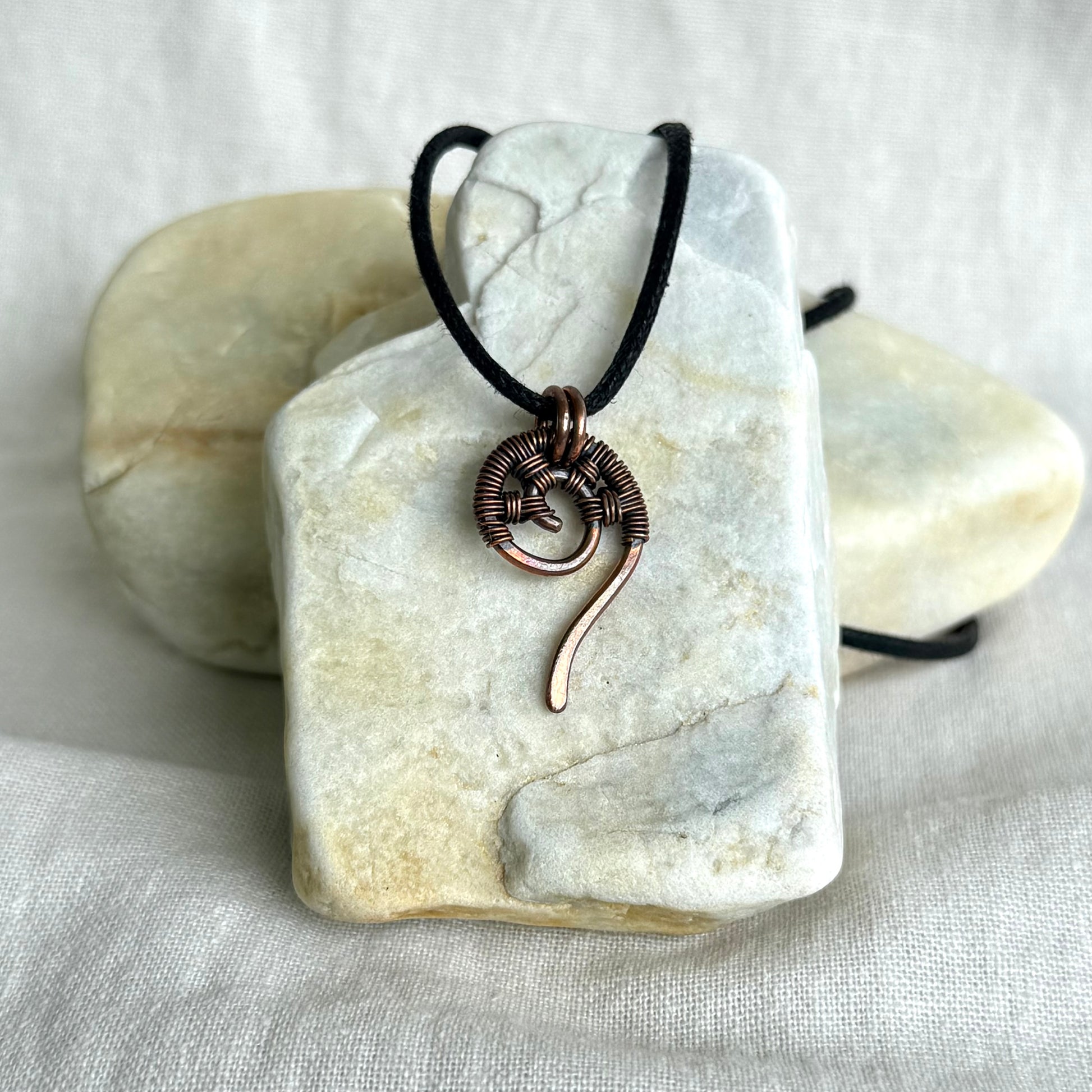 Copper wire-wrapped pendant on a black cord, displayed on a white stone surface.
