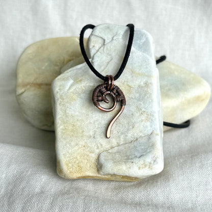 Copper wire-wrapped pendant on a black cord, displayed on a white stone surface.