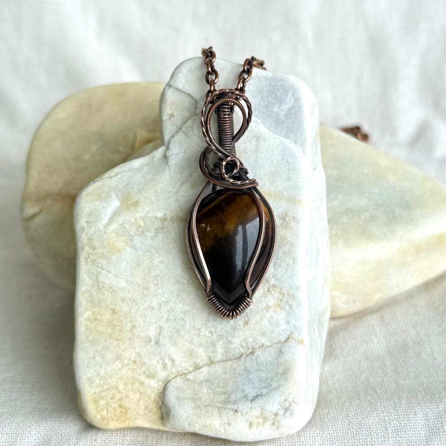 Copper pendant with tiger eye stone on a piece of stone on linen background