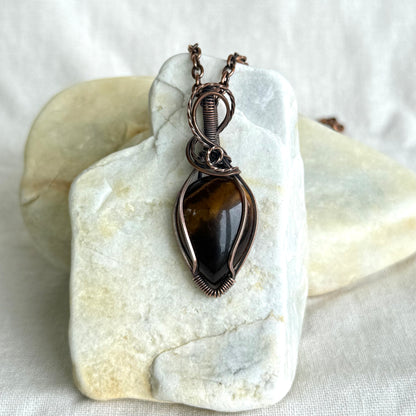 Copper pendant with tiger eye stone on a piece of stone on linen background