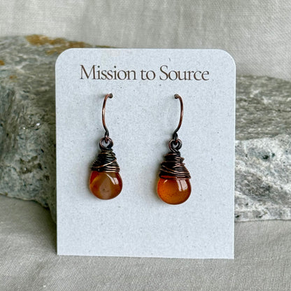Pair of copper and carnelian teardrop earrings on a 'Mission to Source' card with a stone background