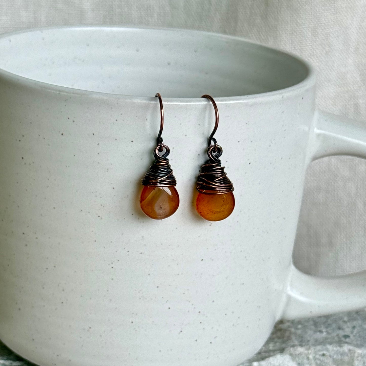 Pair of copper and carnelian teardrop earrings on a white ceramic cup