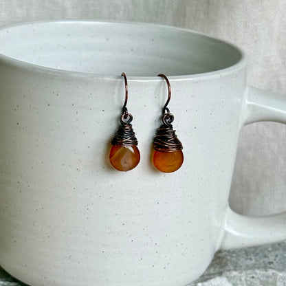 Pair of copper and carnelian teardrop earrings on a white ceramic cup