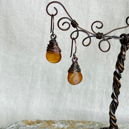 Pair of copper and carnelian teardrop earrings on a decorative stand on linen background