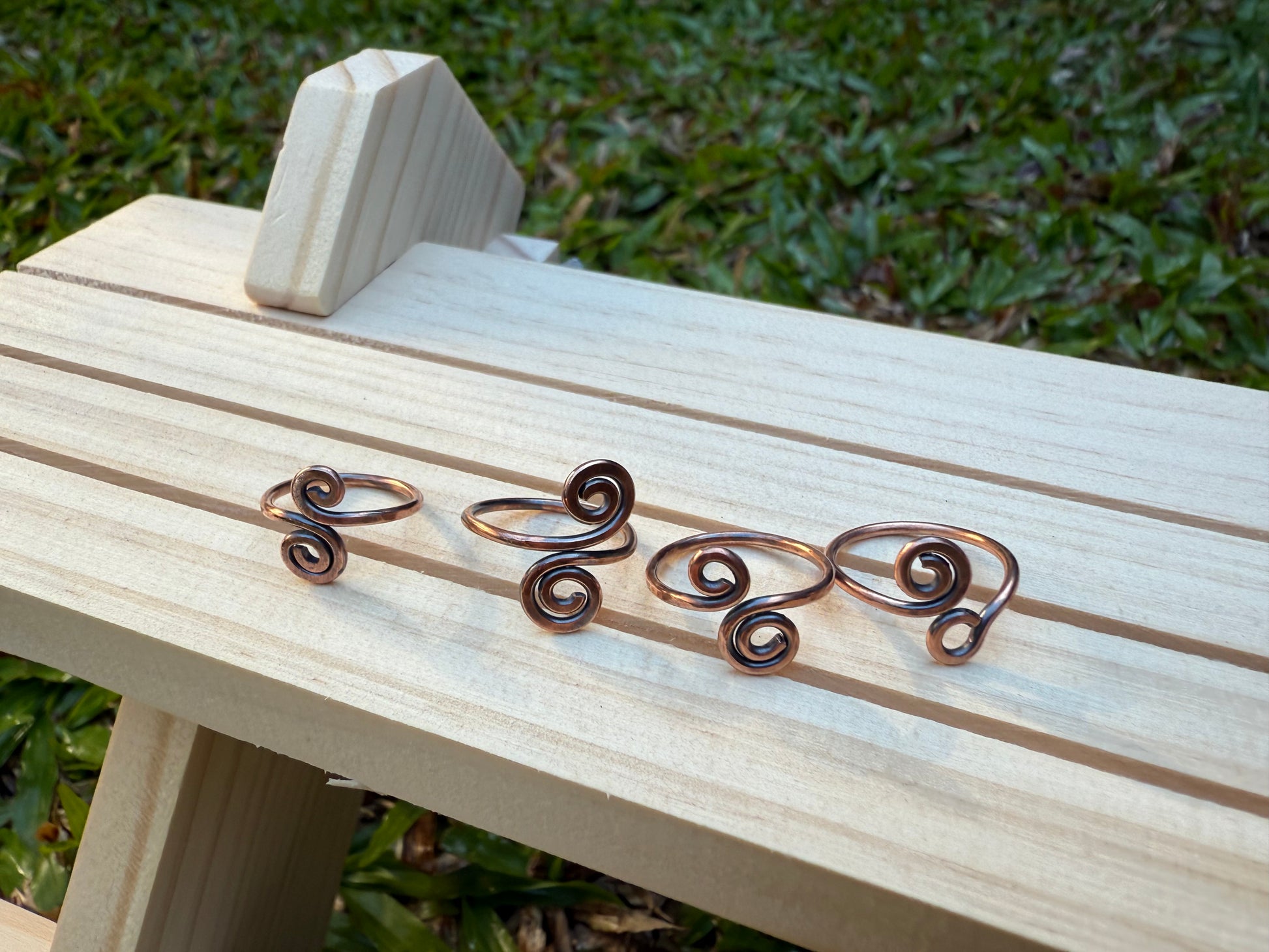 Copper spiral toe rings on a wooden bench with grass in the background