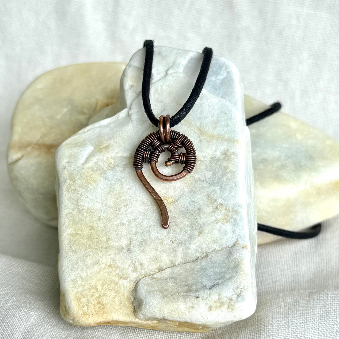 Copper wire-wrapped pendant on a black cord, displayed on a white stone surface.
