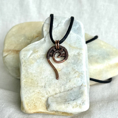 Copper wire-wrapped pendant on a black cord, displayed on a white stone surface.