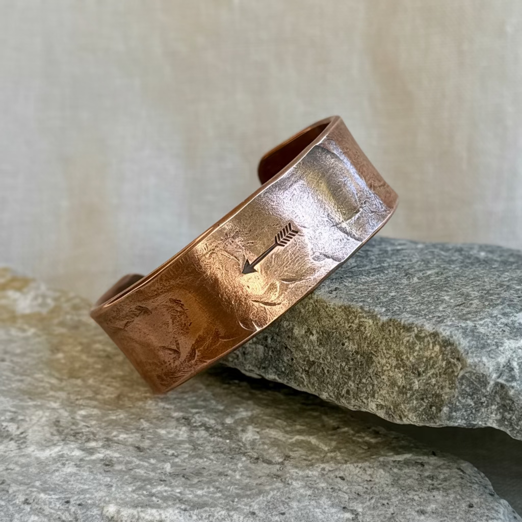 Copper bracelet with stamped arrow on it, leaning on a stone on linen background