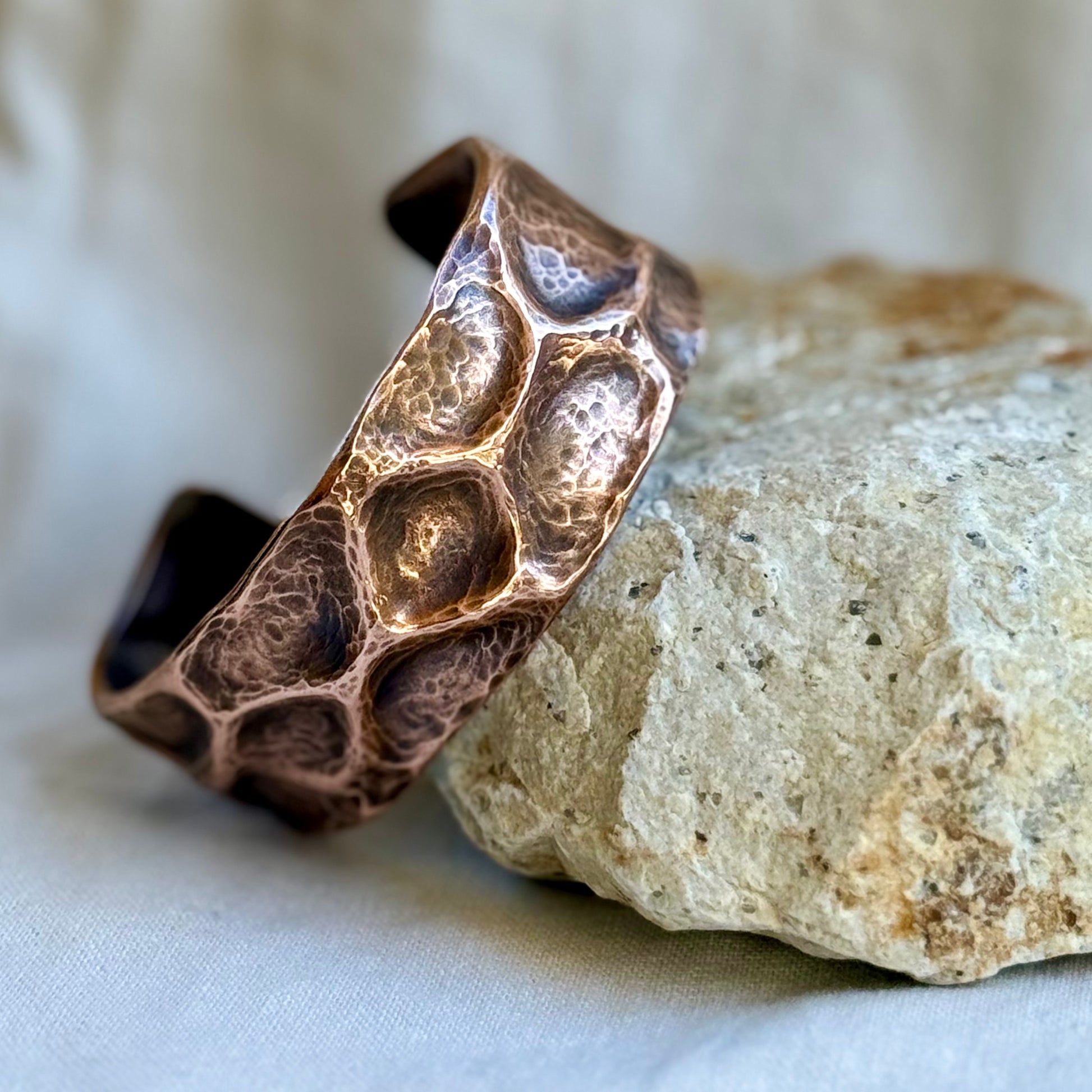 copper cuff with textured surface leaning on a stone with cream background