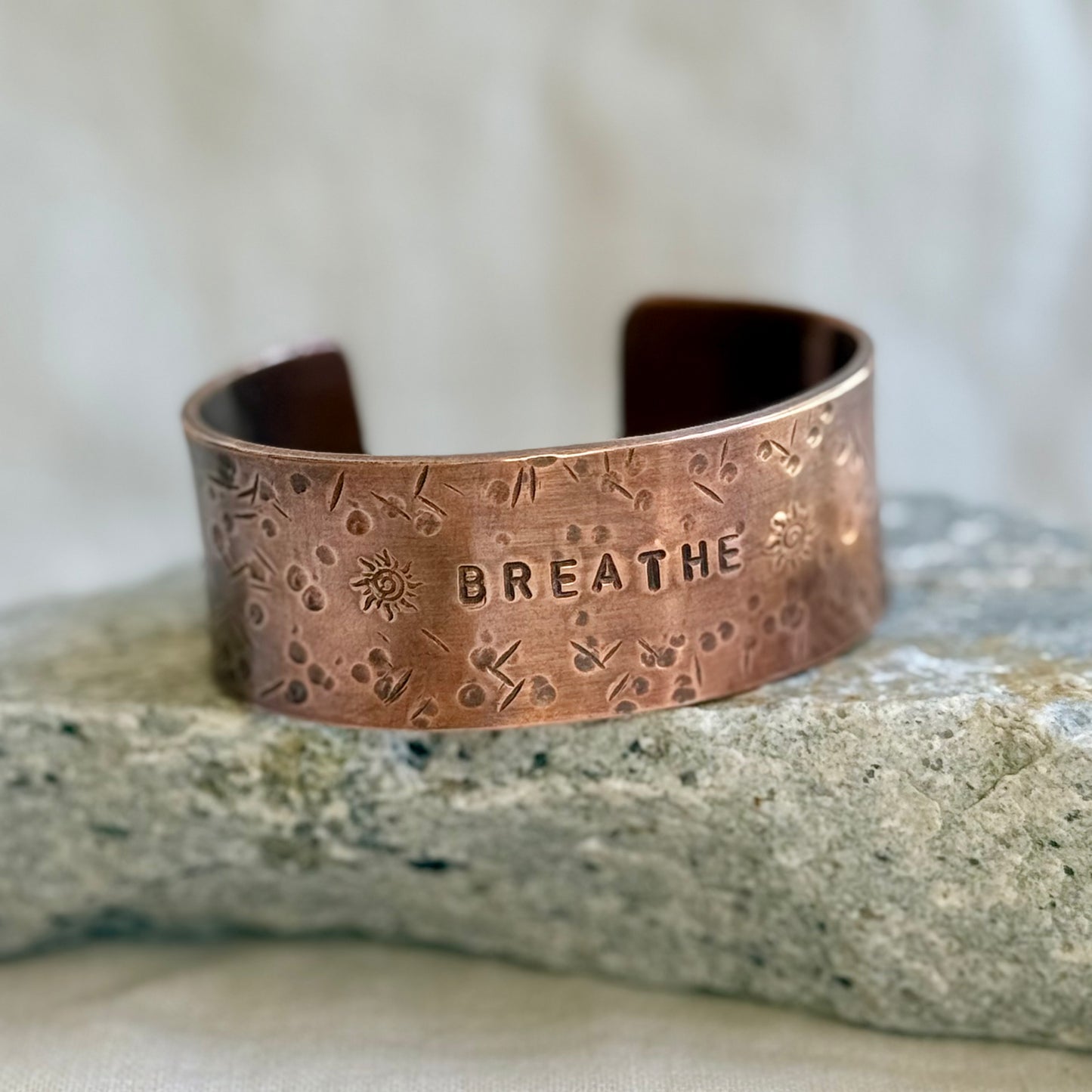 Copper cuff with 'BREATHE' engraving on a stone surface