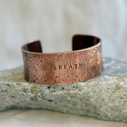 Copper cuff with 'BREATHE' engraving on a stone surface