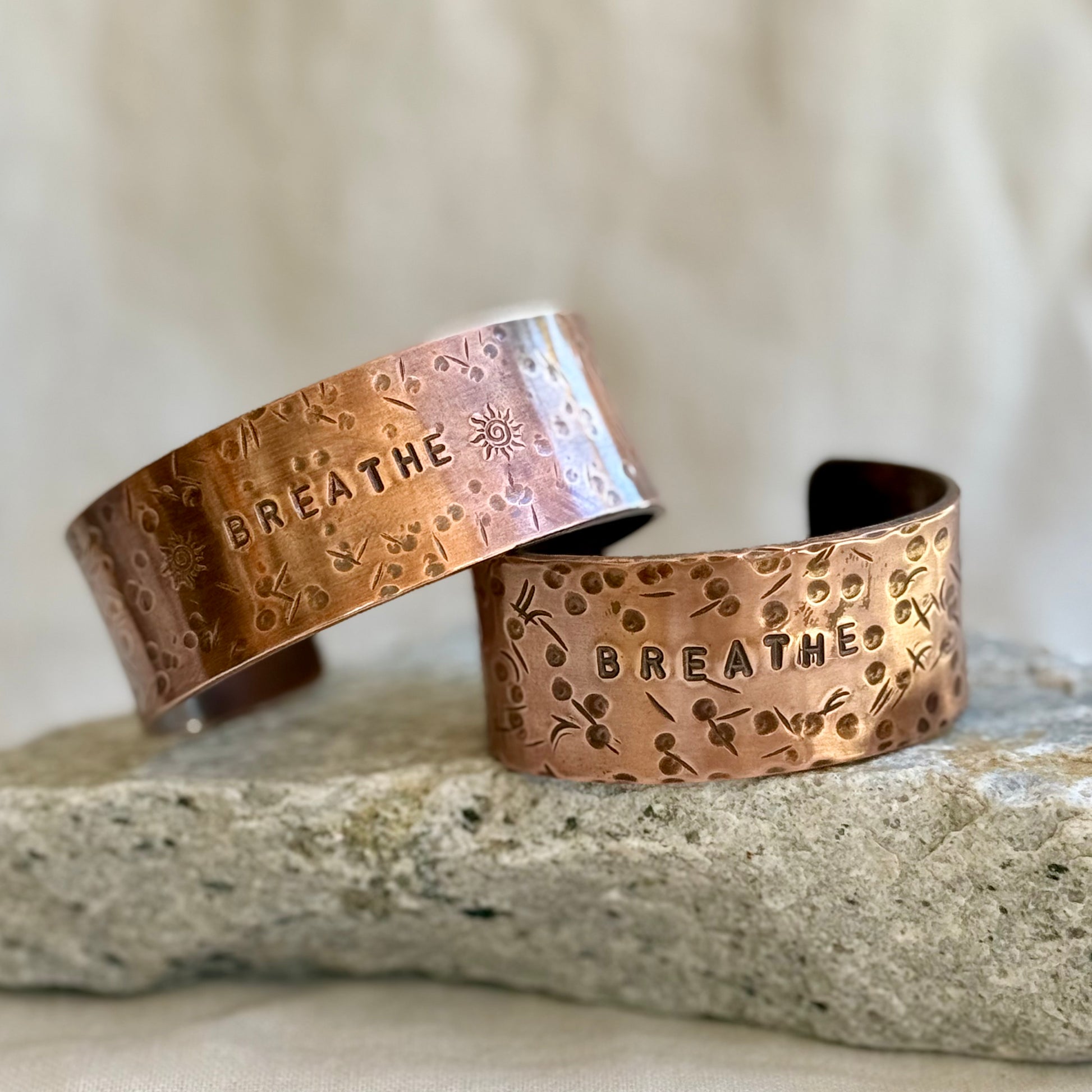 Two copper bracelets with 'BREATHE' engraving on a stone surface.