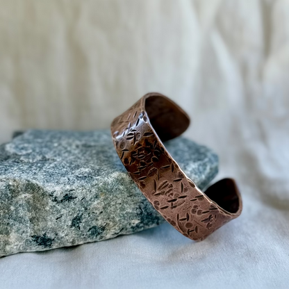 Copper cuff with textured design on a stone surface on cream background