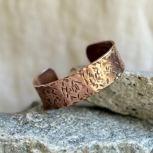 Copper bracelet with textured design on a stone surface with cream background