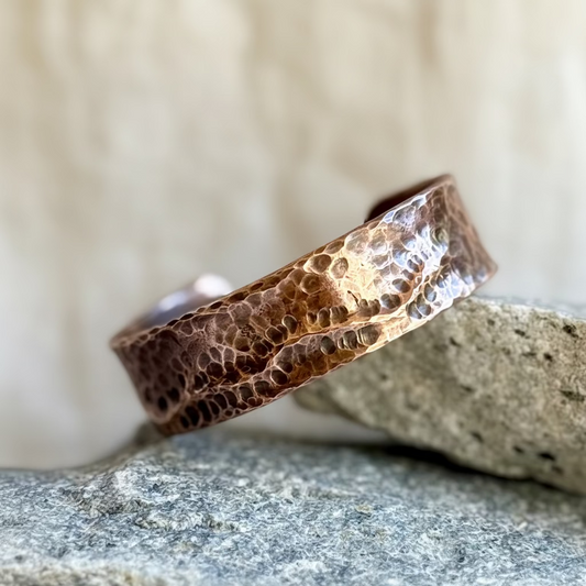 Hammered copper cuff on a stone surface with a blurred background