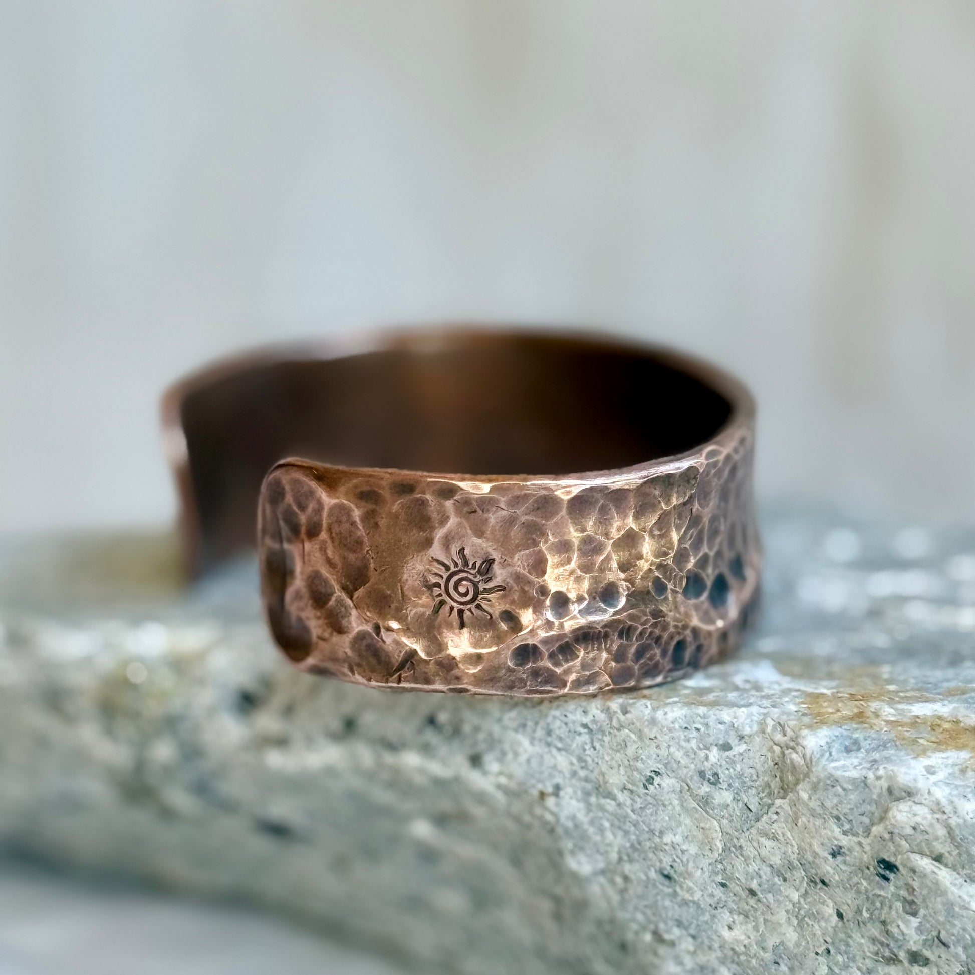 Hammered copper cuff with a sun design on a stone surface