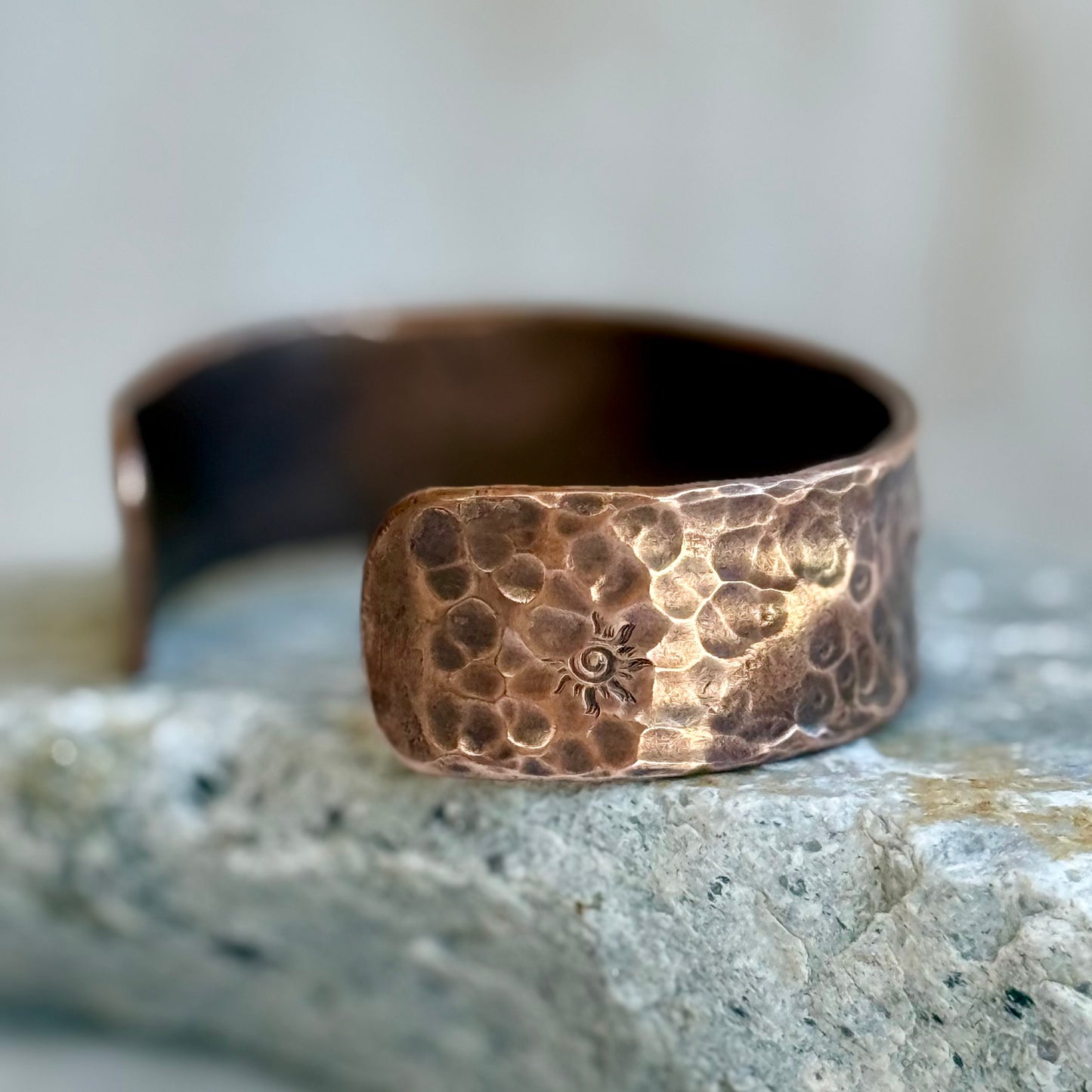 Copper bracelet with textured surface and engraved design on a stone surface