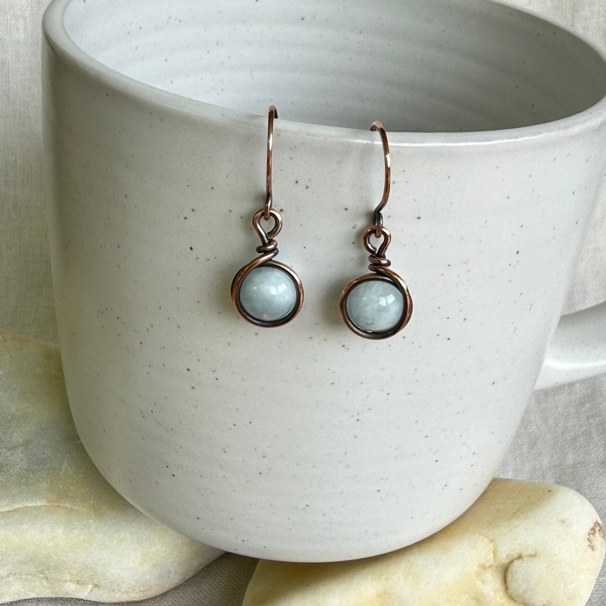Pair of earrings with round gemstones in a white cup on a textured surface