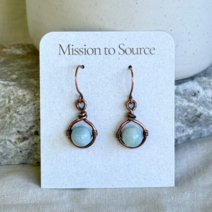 Pair of copper earrings with light blue round stone on a 'Mission to Source' card with a stone background