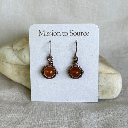 Pair of earrings on a 'Mission to Source' card with a stone background