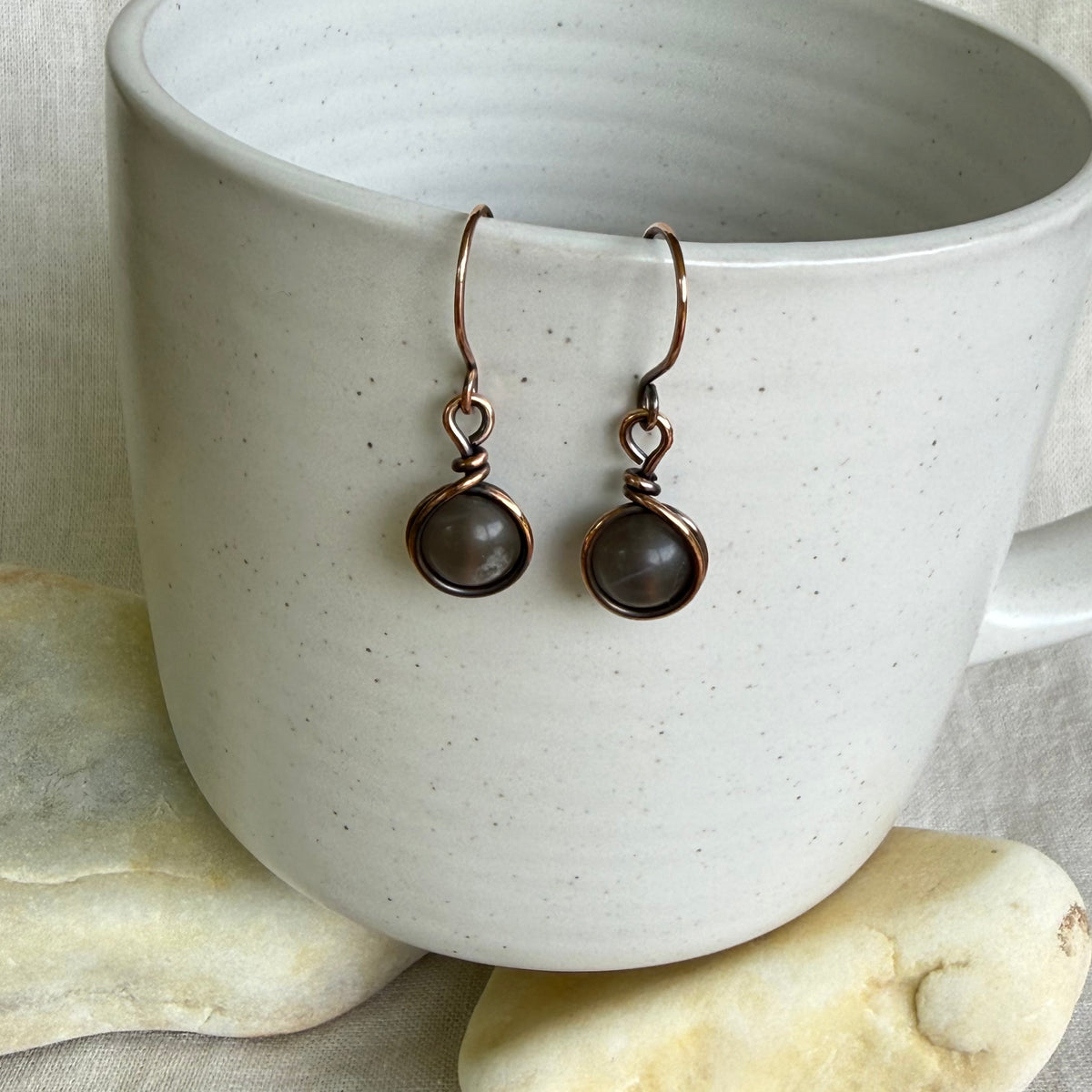 Pair of copper earrings hanging on a white ceramic cup.