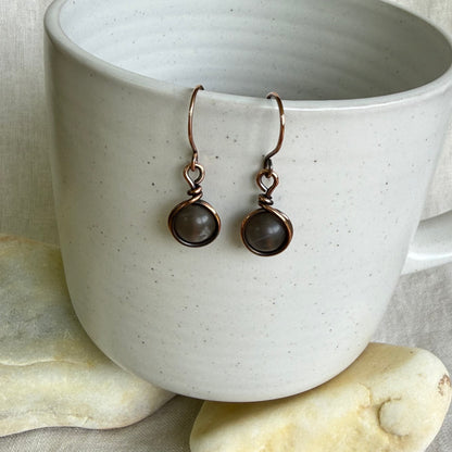 Pair of copper earrings hanging on a white ceramic cup.