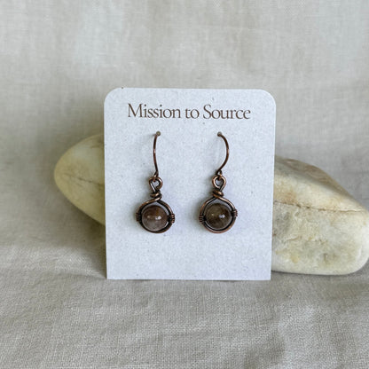 Pair of copper earrings with brown gemstones on a 'Mission to Source' card with a stone background