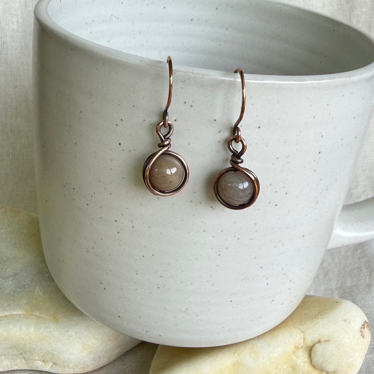 Pair of earrings with round gemstones on a white ceramic cup