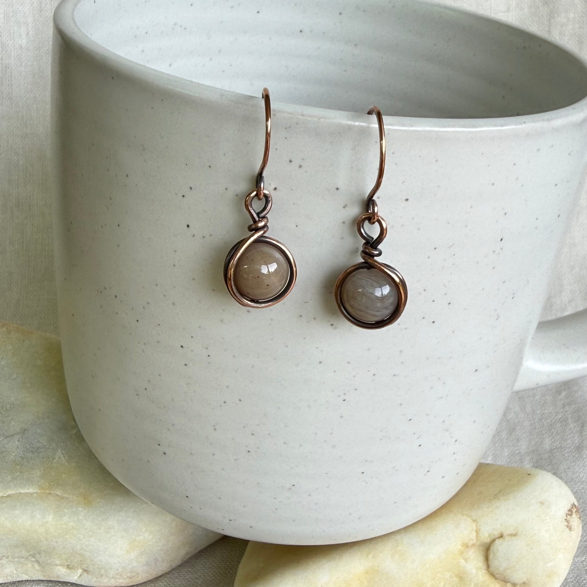 Pair of earrings with round gemstones on a white ceramic cup