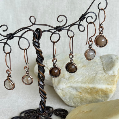 Set of earrings hanging from a decorative metal stand with a stone background