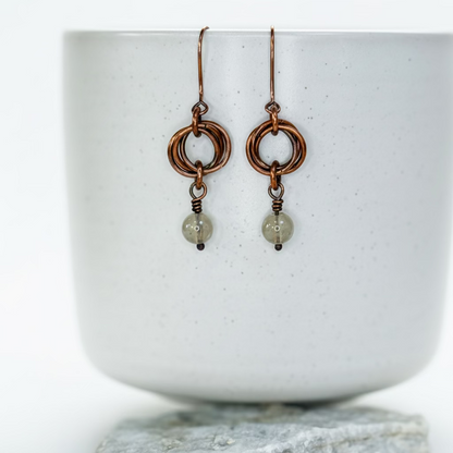 Pair of copper earrings with Golden Rutile beads on a white ceramic surface