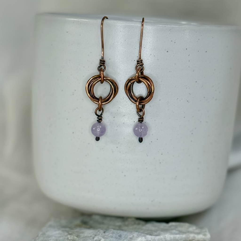 Pair of copper earrings with purple Kunzite beads on a white ceramic mug.