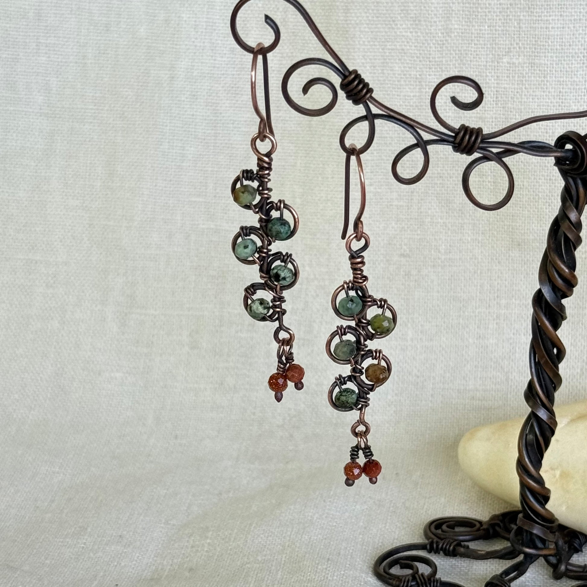 Pair of earrings with green and brown beads on a decorative stand against a light background