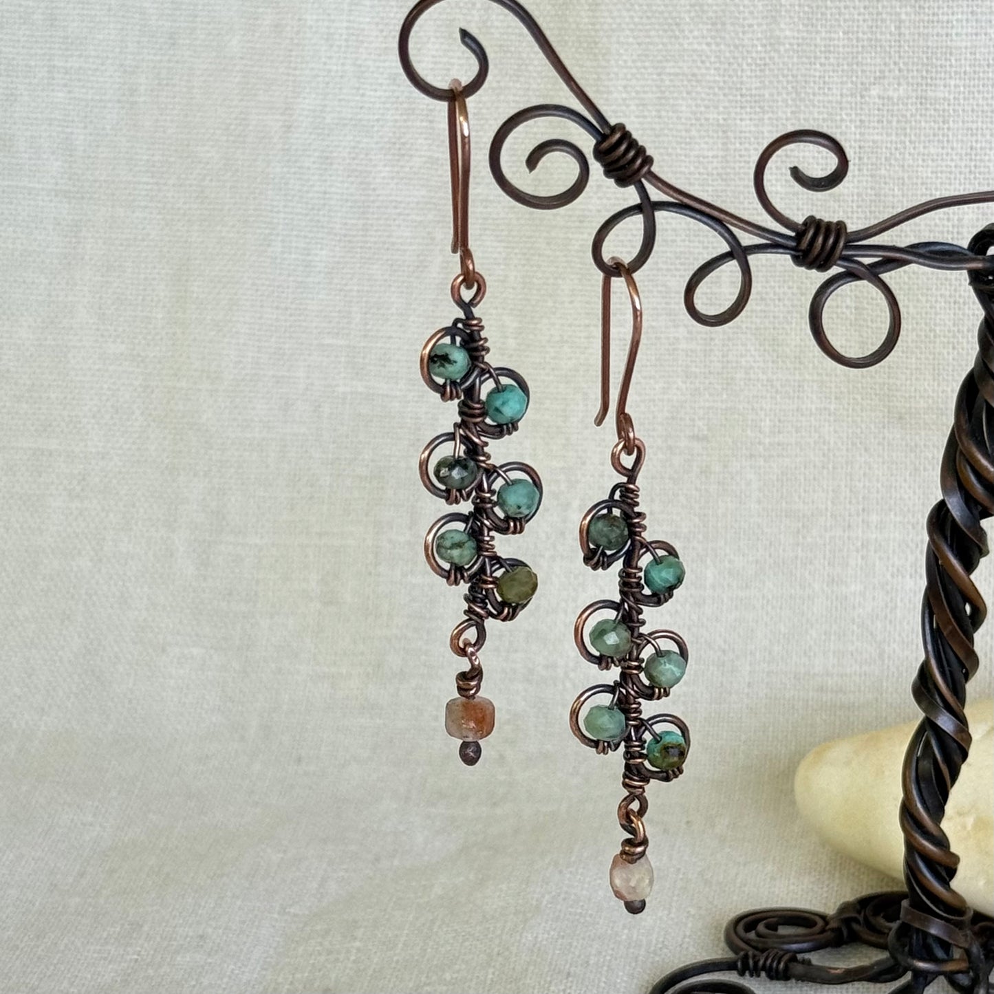 Pair of earrings with green beads hanging on a decorative stand.