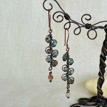 Pair of earrings with green beads hanging on a decorative stand.