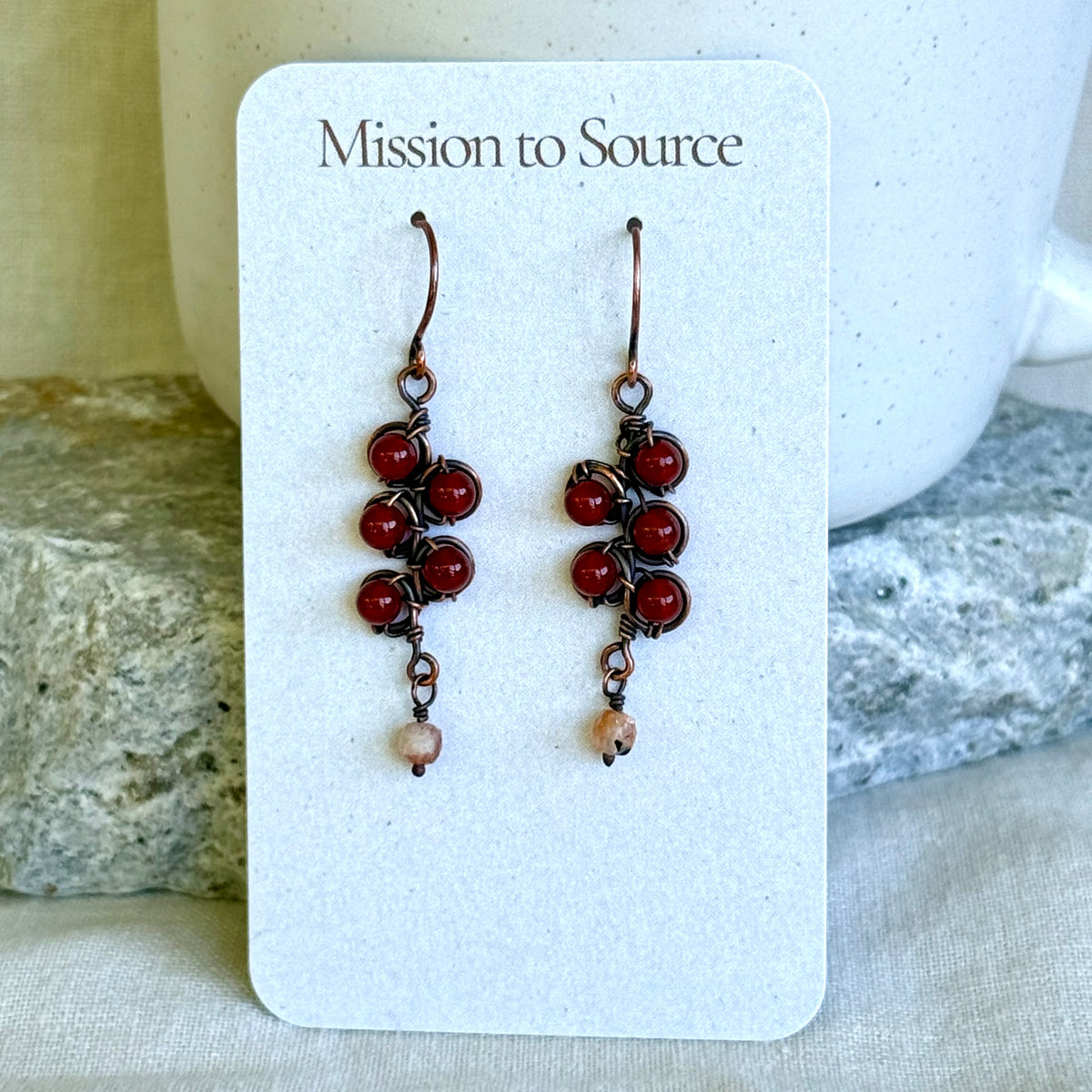 Pair of red beaded copper earrings on a 'Mission to Source' card with a neutral background.