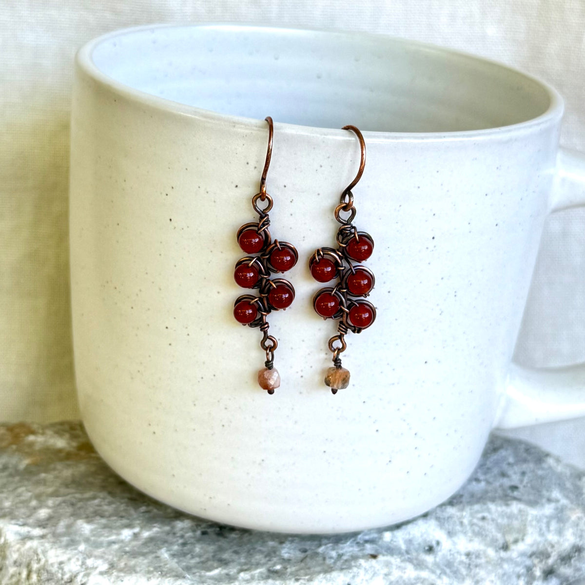 Pair of red beaded earrings hanging over a white mug.
